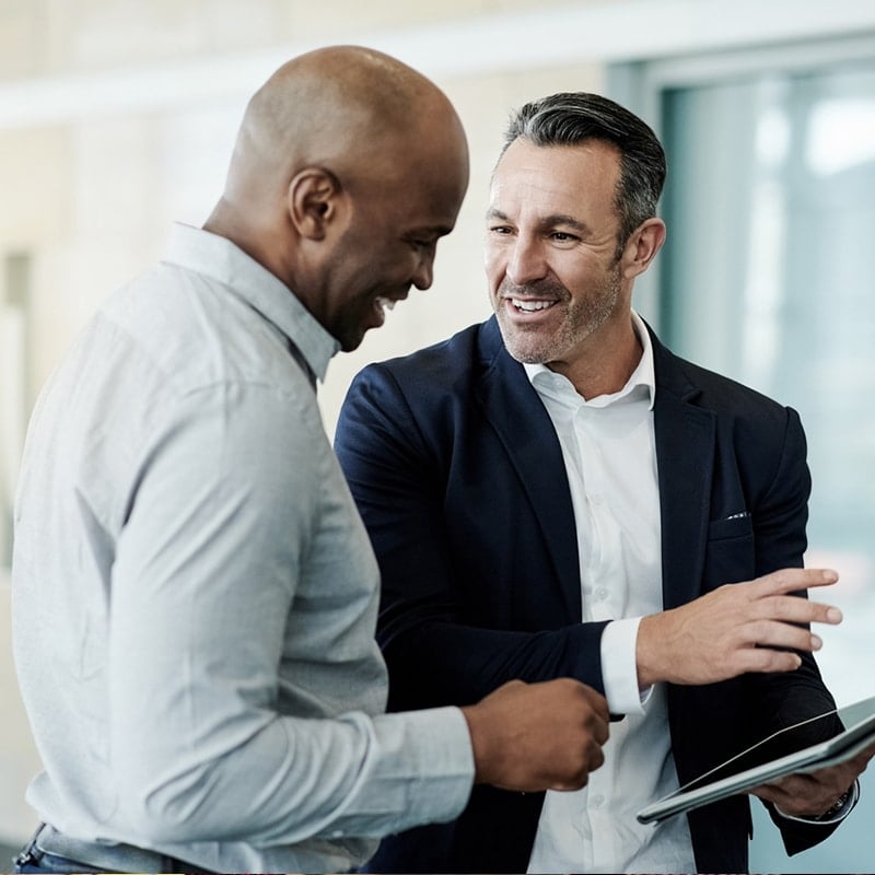 A white businessman and a black businessman having a conversation while holding an iPad.