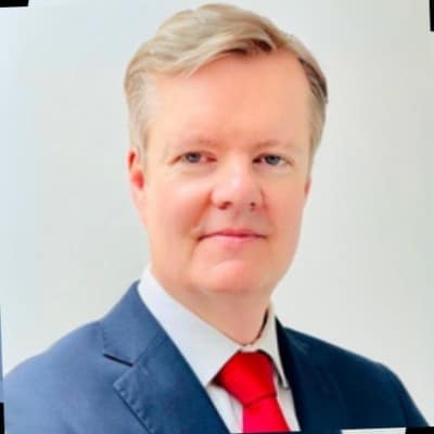 Richard Steward's headshot cropped to show his head and shoulders, he has short hair neatly styled and looks towards the viewer wearing a suit with a white shirt and red tie.