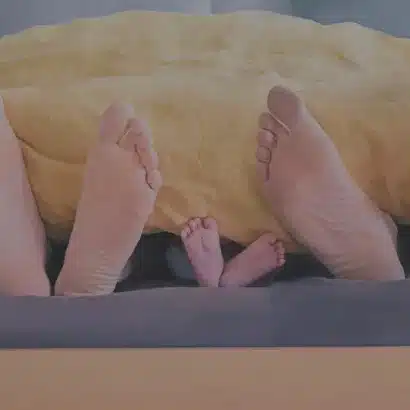 Feet sticking out of the end of a duvet. There are three pairs of feet, two adults and one childs.