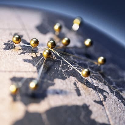 A black and white map of Europe, with gold pins stuck in at various places and string looped around them.