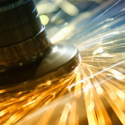 A close up of machinery working on metal, with sparks flying off it.