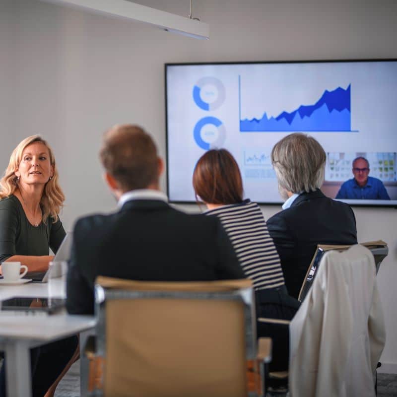 Group of people sat around a boardroom table, looking a screen that is showing a lot of data.