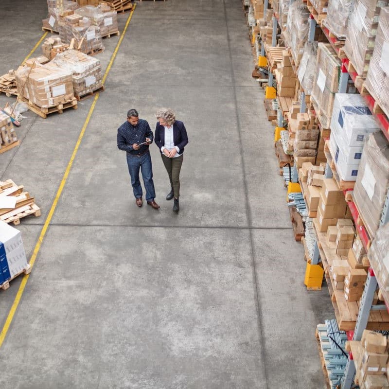 Two people standing in a warehouse, having a conversation over an iPad.