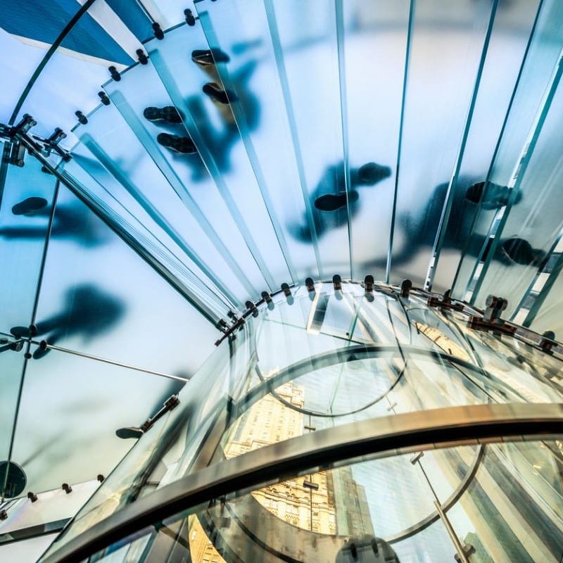 People walking on a see through staircase, with the camera looking at them from below.