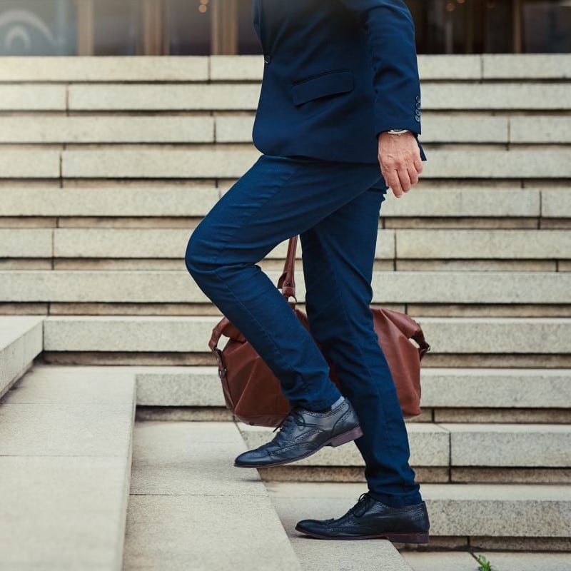 Business man in a blue suit, climbing some stairs, carrying a brown leather bag.