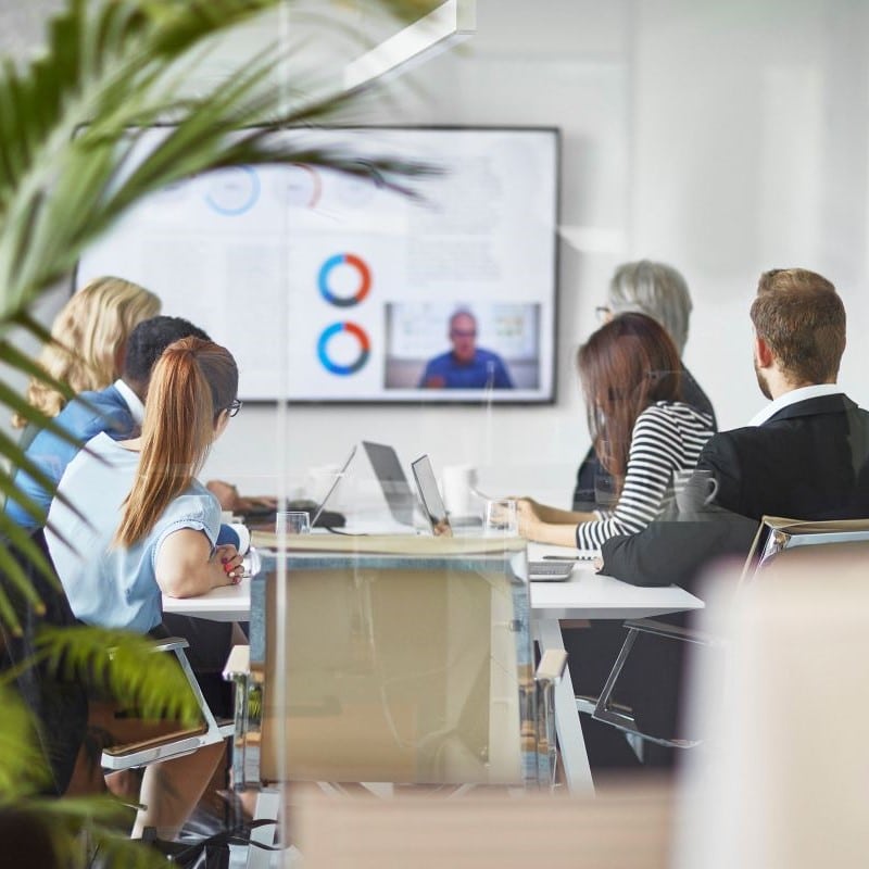 Group of business professionals sat around a board room looking at some data on the main screen.