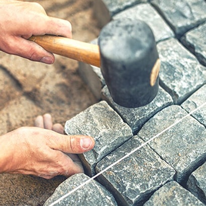 A mallet above small stones that are being laid as part of a path.