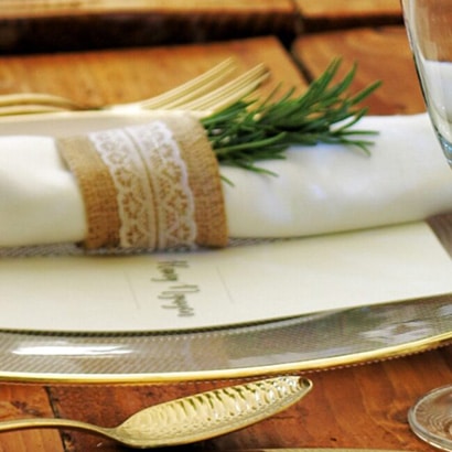 A napkin with a decorative ring holding rosemary is placed on top of a plate on a decorated wooden table.