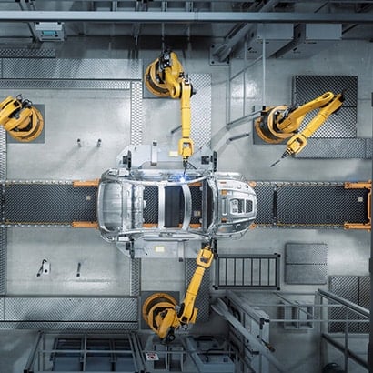 A car manufacturing production line, with robotic arms working on the outer shell of a silver car.