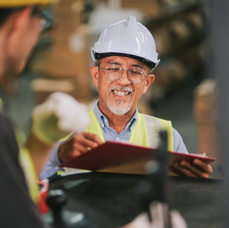 A man with a white hard hat and high vis vest holding a red clipboard
